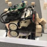 Thymio II Roboter mit einer Schaufel aus Legosteinen, der Holzwürfel schiebt